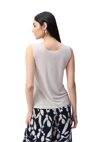 Woman wearing a white sleeveless top and patterned pants on a light gray background