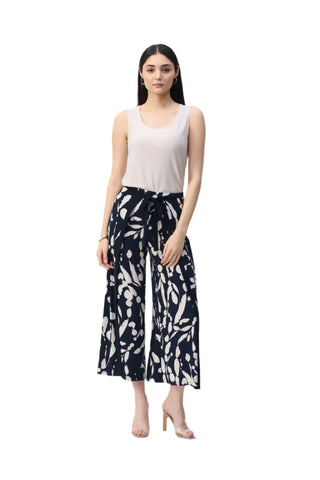 Woman wearing a white sleeveless top and black and white patterned pants on a white background
