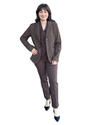 Woman in a brown suit standing in front of a brick building with decorative hay bales and flowers.