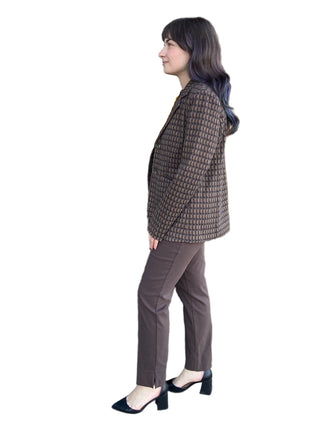 Woman in a brown checkered jacket and pants standing in front of a store with decorative flowers.