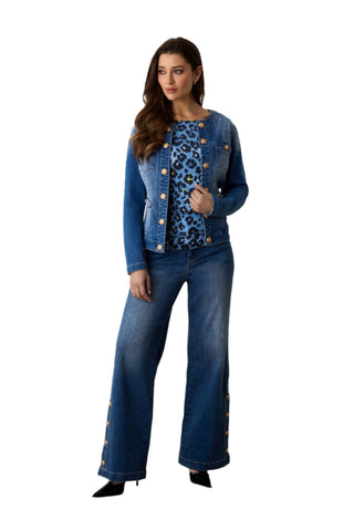 Woman wearing a blue denim outfit with leopard print top, standing in a minimalistic room.