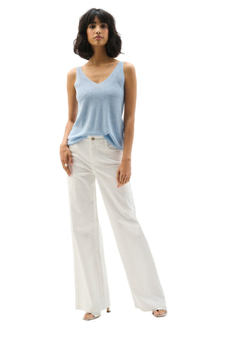 Woman wearing a light blue sleeveless top and white pants on a white background