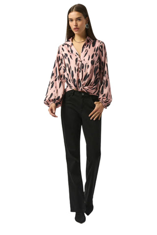 Woman wearing a pink blouse with black patterns and black pants on a white background