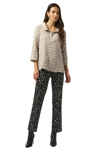 Woman wearing a textured beige top and patterned black pants on a white background
