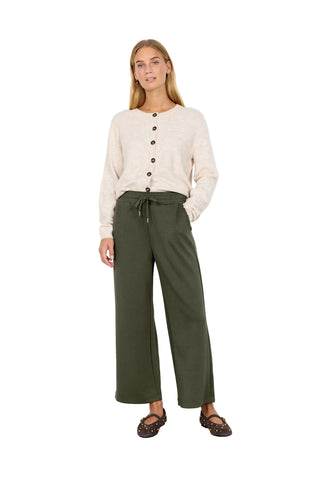 Woman wearing a beige sweater and green pants against a white background