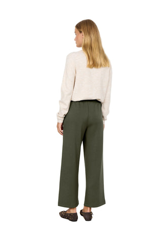 Woman wearing a beige sweater and green pants against a white background