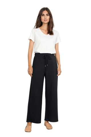 Woman wearing a white top and black wide-leg pants against a white background