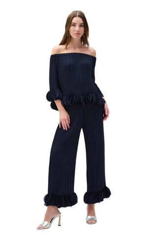 Woman wearing a navy blue off-shoulder top and wide-leg pants on a white background
