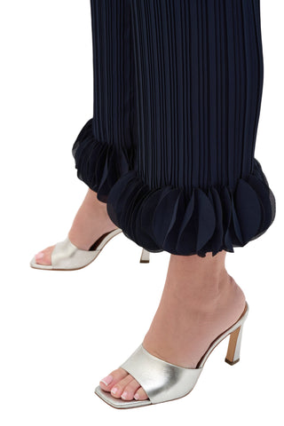 Silver high-heeled sandals worn with navy pleated pants on a white background