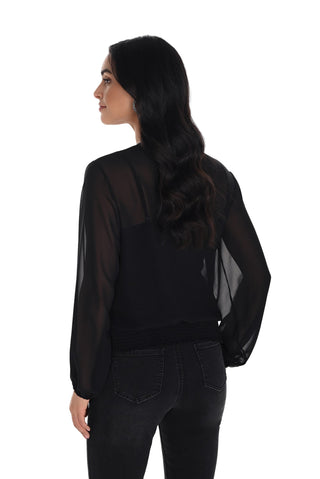 Woman wearing a black sheer blouse and dark jeans on a white background