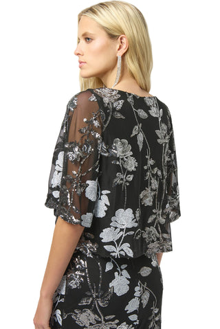 Woman wearing a black floral blouse with sheer sleeves on a white background