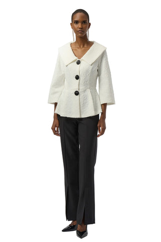 Woman wearing a white jacket with black buttons and black pants on a white background