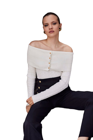 Woman wearing a white off-shoulder top with buttons and black pants sitting on stone steps.