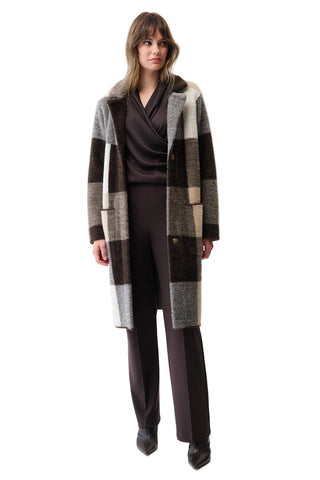 Woman wearing a long, checkered coat over a dark outfit on a white background