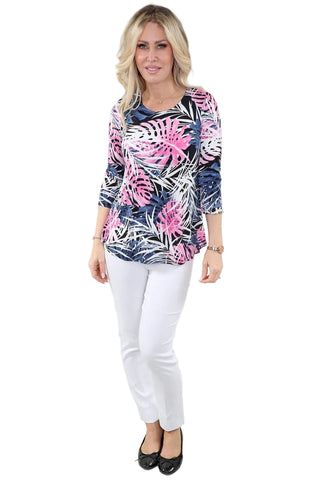 Woman wearing a colorful leaf-patterned top and white pants on a plain background