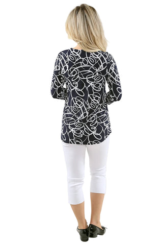 Woman wearing a black and white patterned top with white pants on a light gray background