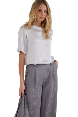 A woman modeling a white short-sleeve top and gray wide-leg patterned trousers against a plain light gray studio background.