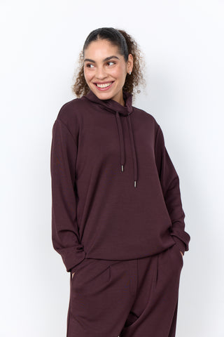 Woman wearing a maroon hoodie and pants on a white background