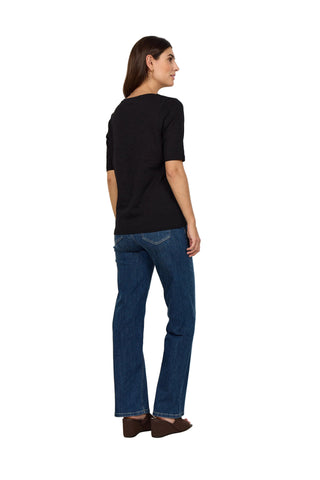 Woman wearing a black top and blue jeans against a white background