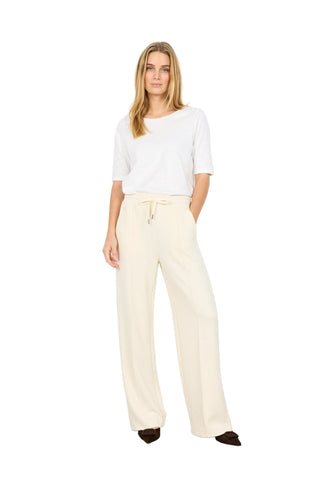 Woman wearing a white top and beige pants against a white background