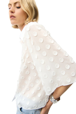 Woman wearing a white blouse with large polka dots on a plain background