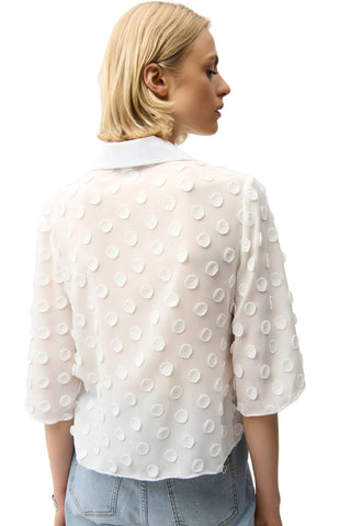 Woman wearing a white polka dot blouse against a plain background