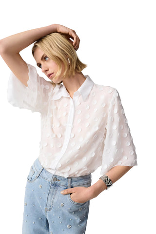 Woman wearing a white blouse with polka dots and light blue jeans on a gray background