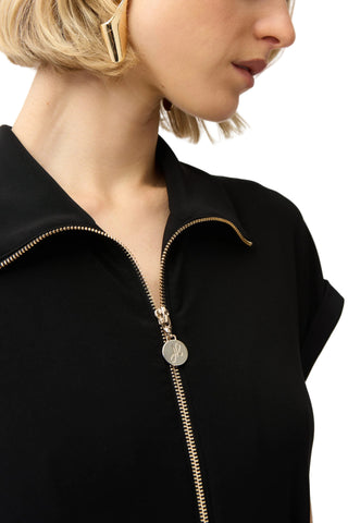 Close-up of a black jacket with a gold zipper on a plain background