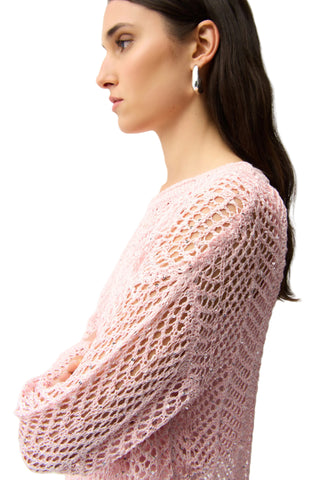Woman wearing a pink crochet sweater against a plain background