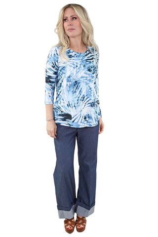 Woman wearing a blue tie-dye top and dark pants on a plain background