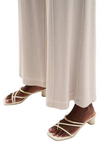 Pair of strappy sandals worn with beige pants on a white background