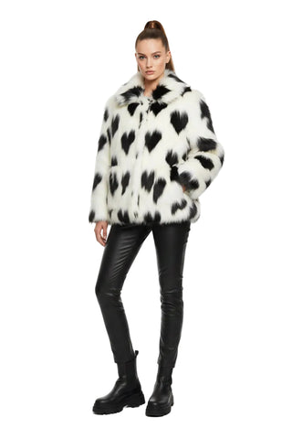 A black and white cow-print faux fur jacket with a collar and front buttons, hanging in a retail store.