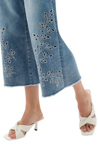 Denim pants with floral embroidery and white sandals on a white background