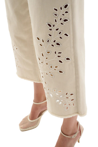 Beige pants with cut-out leaf pattern worn by a person on a white background