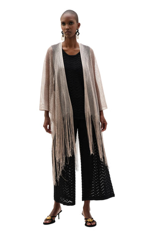 Woman wearing a long beige scarf with fringe, black top, and wide-leg pants on a white background