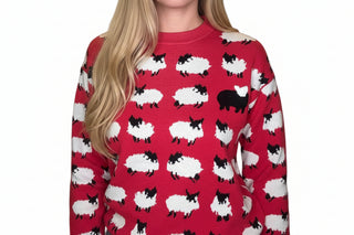 A person wearing a red crewneck sweater with an all-over black and white sheep print, featuring a larger black sheep motif on the left chest. The photo is cropped from the neck down, showing the sweater's texture and pattern clearly.