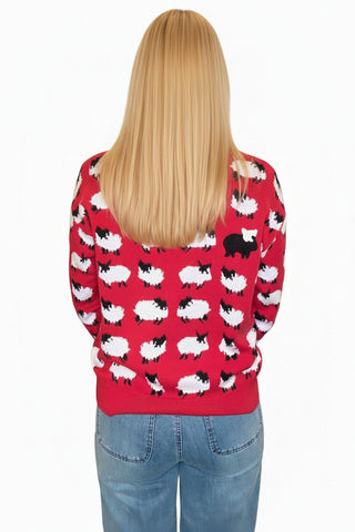 A woman viewed from behind wearing a bright red sweater with a repeating black and white sheep pattern, paired with light blue jeans in an indoor hallway setting.