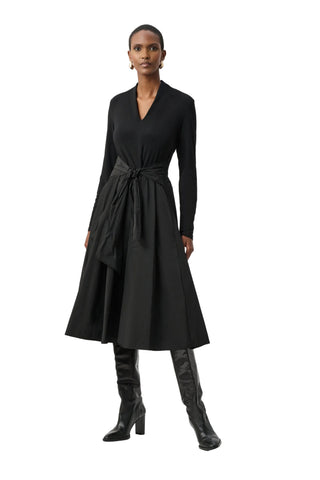 Woman wearing a black dress with a belt and black knee-high boots on a white background
