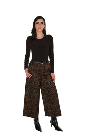 A woman modeling a dark brown long-sleeve top and wide-leg leopard-print pants with a black belt and black pointed-toe boots, standing against a plain white studio background.