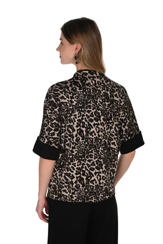 A woman shown from the back wearing a short-sleeve leopard print blouse with black cuffs and black trousers, photographed against a plain white studio background.