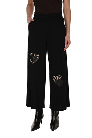 Black pants with heart-shaped cutouts worn by a person on a white background