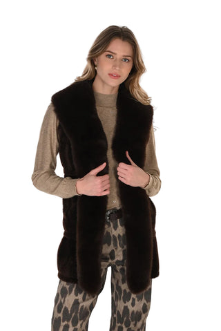 Woman wearing a brown fur vest over a beige sweater and leopard print pants on a white background