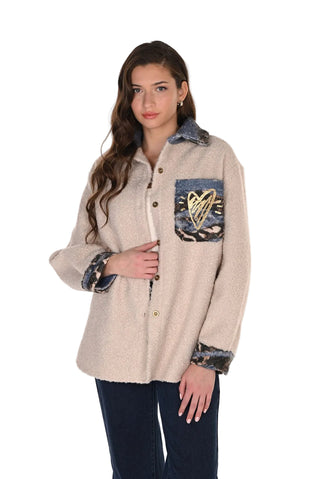 A woman modeling a beige sherpa button-up jacket with blue patterned pocket and cuffs, featuring a gold heart design on the pocket, set against a plain white background.