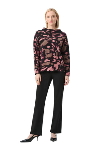 Woman wearing a pink and black patterned top with black pants on a white background