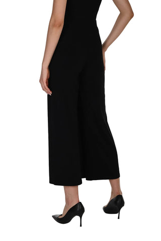 A model wearing a black sleeveless wide-leg cropped jumpsuit with black pointed-toe heels, shown from a rear three-quarter angle against a white studio background.