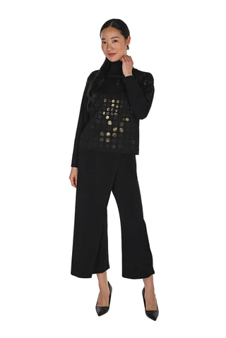 A woman modeling a black outfit consisting of a long-sleeve black top with circular cutout detailing, black wide-leg cropped pants, and black pointed-toe heels, set against a plain white studio background.