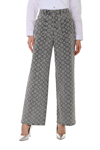 A model is shown from the waist down wearing high-waisted, wide-leg trousers with a gray and white geometric monogram pattern, styled with a white shirt and silver heels.