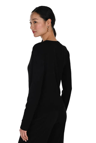 A woman with her hair pulled back is shown from a side-back angle wearing a solid black long-sleeve knit top or dress against a clean white studio background.