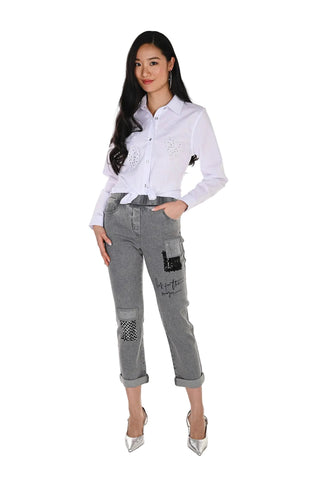 Woman wearing a white shirt and gray jeans with patches on a white background