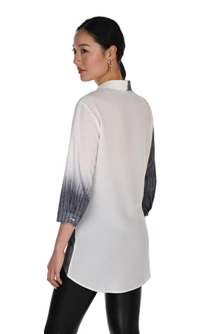 A woman shown from the back wearing a white long-sleeve tunic top with a black-to-white ombré gradient sleeve, paired with black pants, against a plain white studio background.